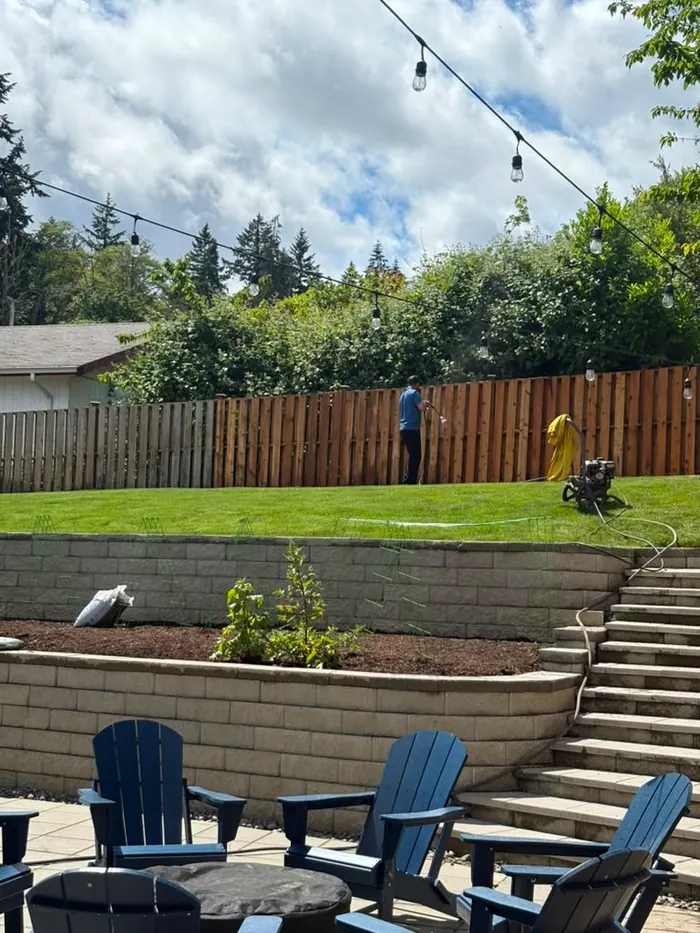 Fence stain being applied along retaining wall in backyard