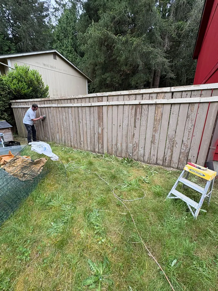 Painter sanding fence boards during exterior prep work